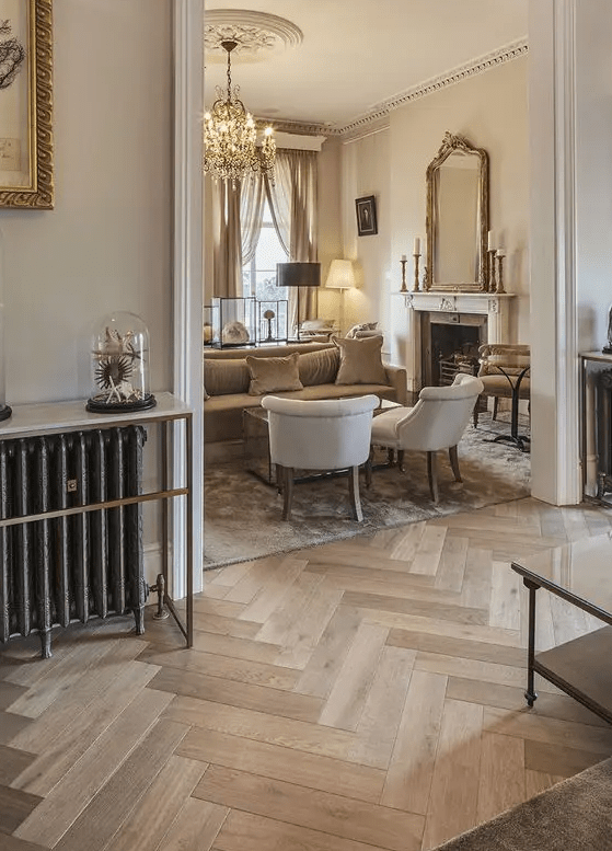 A sophisticated neutral space with light stained herringbone floors, neutral seating furniture, a fireplace and some lamps