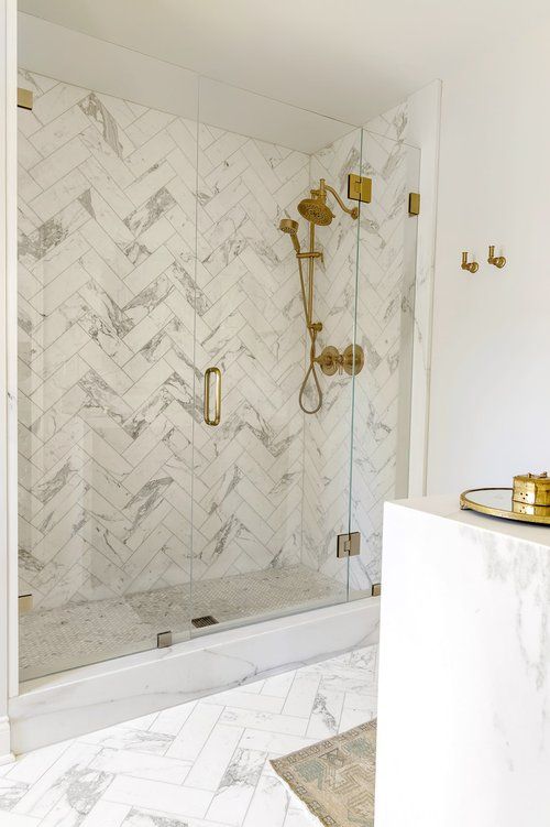 a sophisticated white bathroom clad with marble herringbone tiles, a marble vanity and brass fixtures