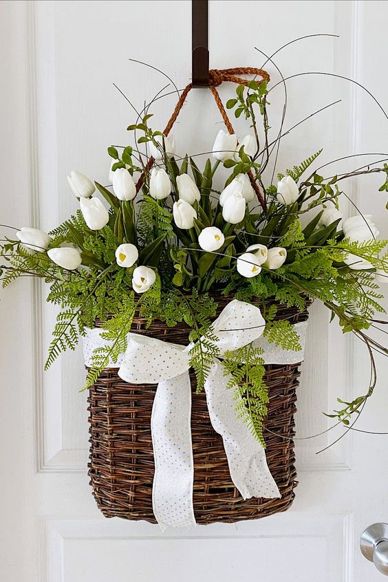a spring door decoration of a basket with a bow, greenery and white tulips, twigs on top is amazing