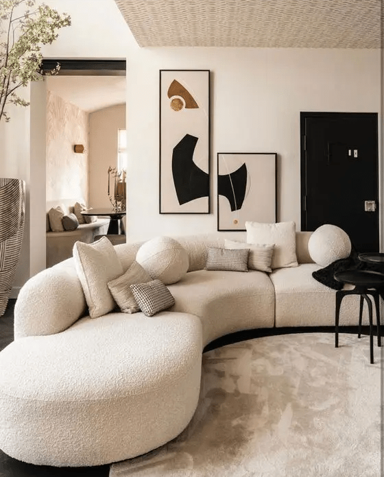 a stylish and contrasting living room with a white boucle curved sofa, a black table and eye-catchy artwork on the wall
