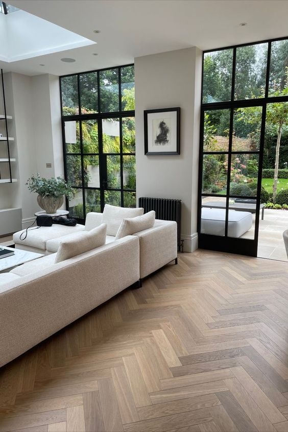 a stylish neutral living room with large windows, a skylight, neutral seating furniture and a gorgeous herringbone floor