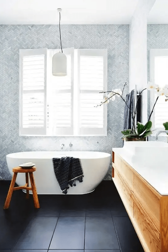 a welcoming modern bathroom with black large scale and light blue herringbone tiles, an oval tub, a timber vanity and dark towels