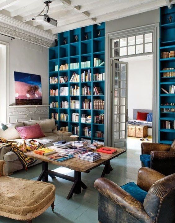a whimsical living room with blue built-in bookshelves, a neutral sofa and brown chairs, a coffee table and some lights and decor