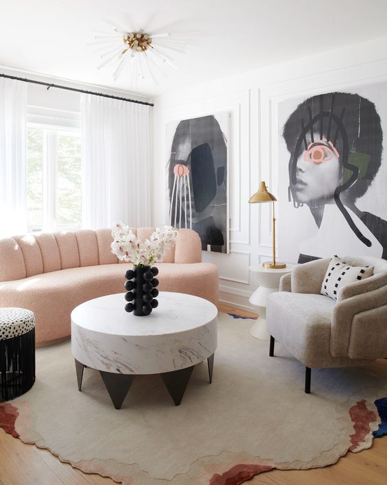 a whimsical living room with oversized artwork, a peachy boucle loveseat, a neutral chair, marble coffee table and brass touches