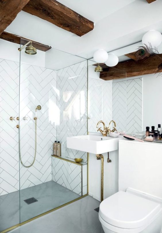 a white bathroom clad with herringbone tiles, dark-stained beams, brass fixtures is a lovely and catchy space