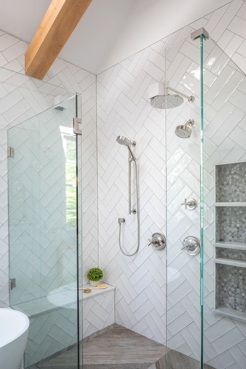 a white bathroom clad with herringbone tiles, with niche shelves, wooden beams and a tub is a cool and catchy space
