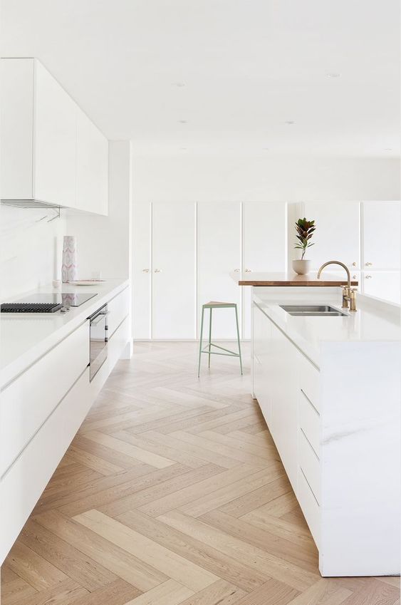 a white minimalist kitchen with a beautiful herringbone floor and just a couple fo details for a super clean look
