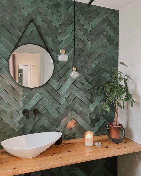 An aesthetic sink space done with green herringbone tiles, a built in wooden vanity and a bowl sink plus hanging bulbs