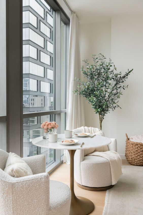 an airy nook by the window with a small table, white boucle chairs, a potted plant is chic, simple and cool