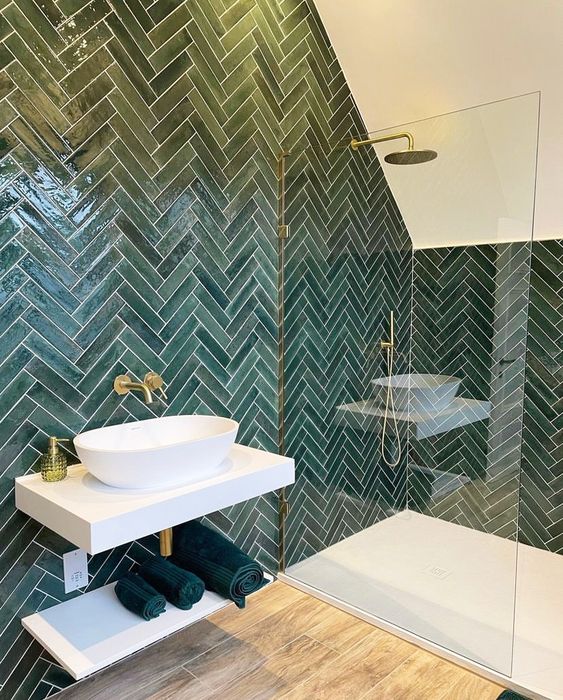 an attic bathroom clad with green herringbone tiles, with a shower space and a floating vanity with a bowl sink