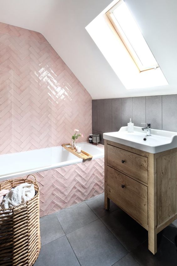 an attic bathroom with a skylight, pink herringbone tiles and grey ones, a stained vnaity and a basket is amazing