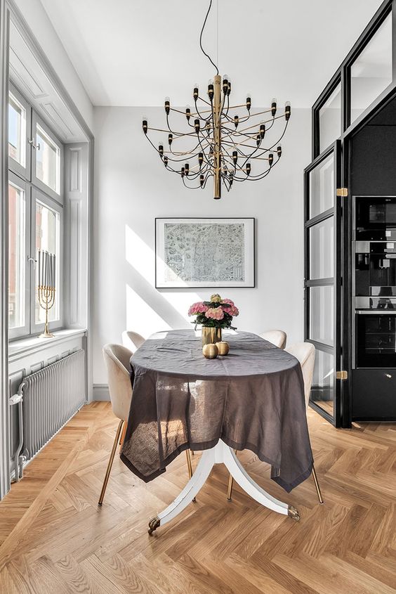 an elegant Scandinavian dining room with white walls and a herringbone floor, a table, neutral chairs and a whimsical chandelier