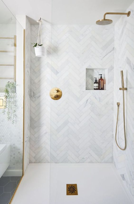 an elegant shower space clad with marble hrringbone tiles, with a niche and brass fixures is cool and catchy