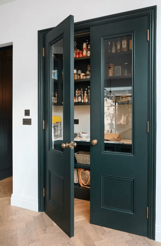 an elegant small pantry with dark green doors, open shelves and baskets, food, drinks and spices
