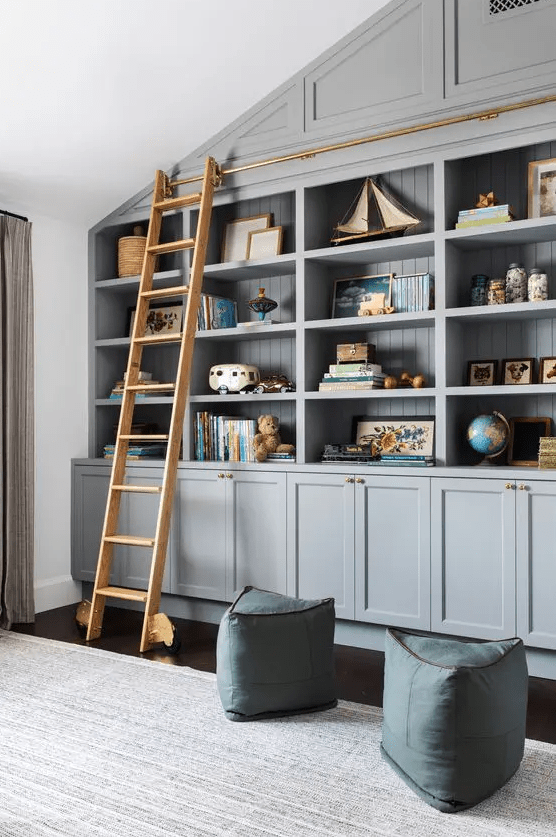 Grey built in bookshelves, blue poufs and a ladder to get all the books comfortably