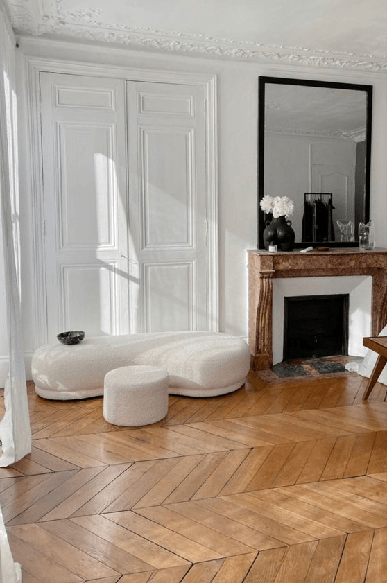 a French chic living room with molding, chevron floors, a fireplace, a boucle seat, a mirror and some decor