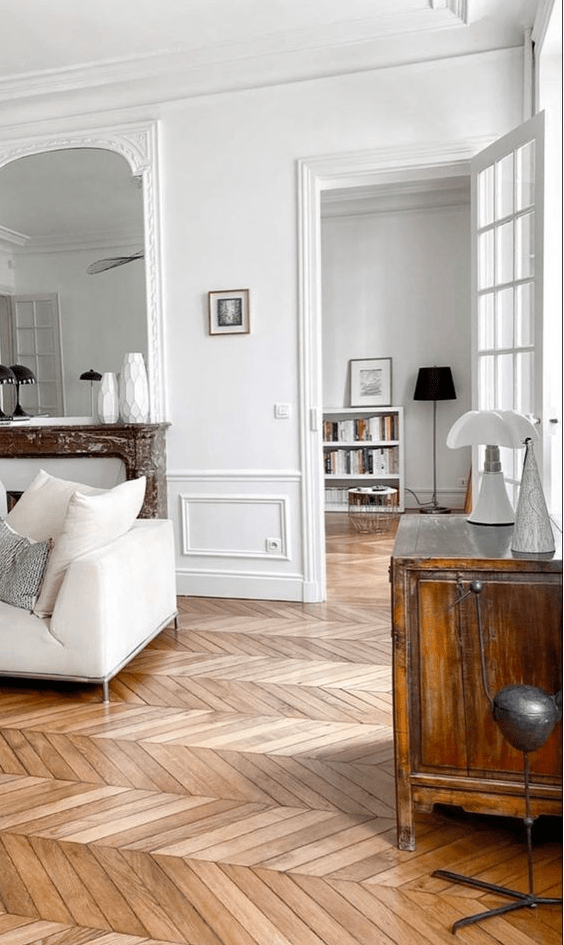 a French chic living room with molding, chevron floors, a white sofa, a fireplace, a credenza and some lamps
