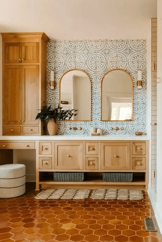 a Mediterranean bathroom with blue printed tiles, a terracotta tile floor, stained cabinets and arched mirrors