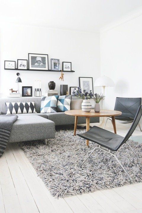 a Scandinavian living room with a grey sectional, a ledge gallery wall, black chairs and a coffee table with decor