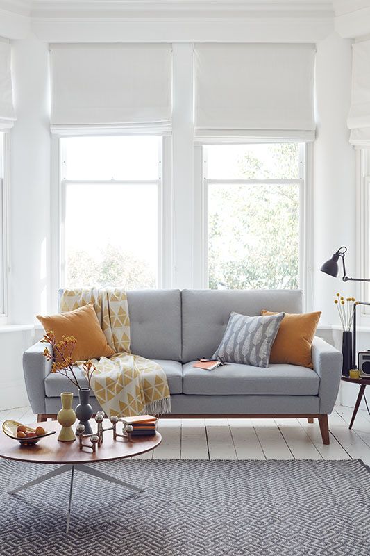 a Scandinavian living room with a grey sofa and yellow pillows, a coffee table and a printed rug and a black lamp