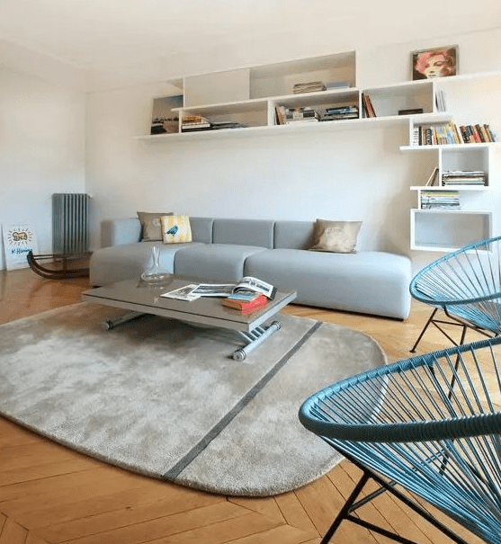 a Scandinavian space wiht a grey low sofa, a grey rug, blue chairs, a low coffee table and a large shelving unit is wow