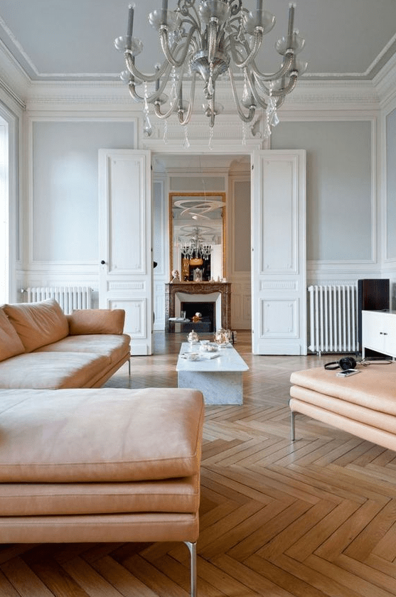 a beautiful Parisian living room with light blue walls and a chevron floor, a peachy sectional and ottoman, a vintage chandelier and a coffee table