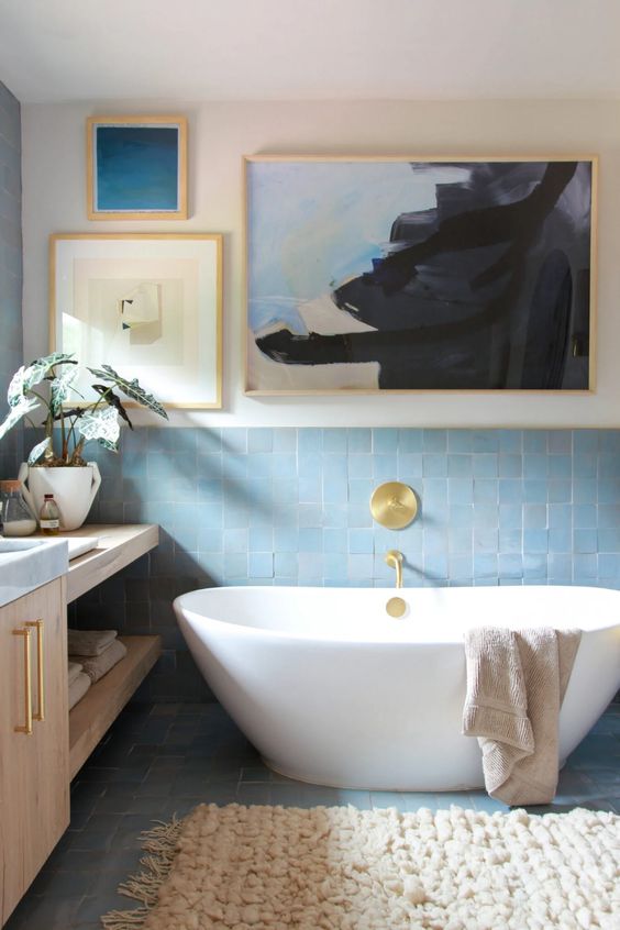 a beautiful coastal bathroom with blue Zellige tile, an oval tub, a stained vanity, a gallery wall and a fluffy rug is ultimate