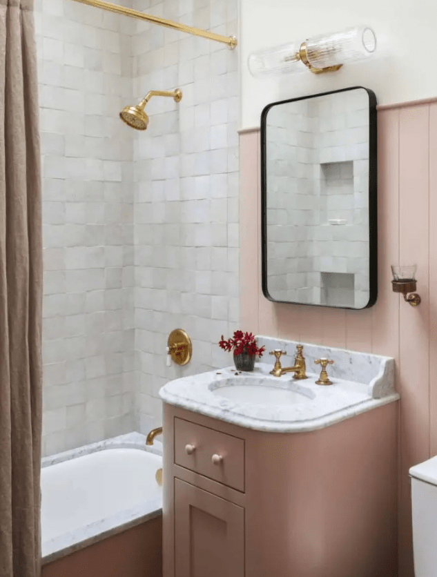 a beautiful modern bathroom with a dusty pink vanity, wall and curtain, white Zellige tiles and gold fixtures