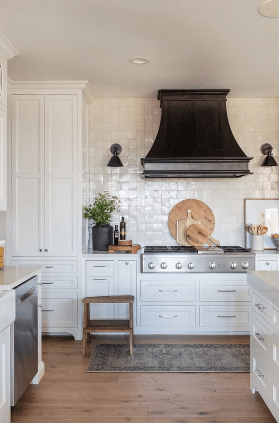 a beautiful white kitchen with shaker cabinets, a white Zellige tile backsplash, a statement black hood and white countertops