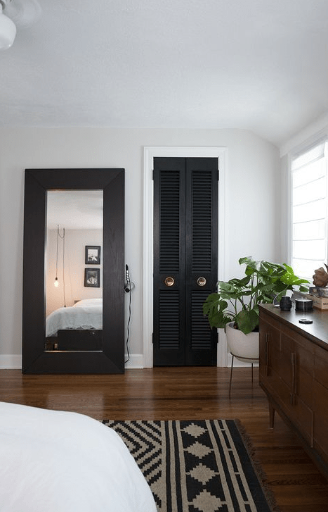 a black shutter door to the closet echoes with a dark wooden frame of the mirror and a printed rug