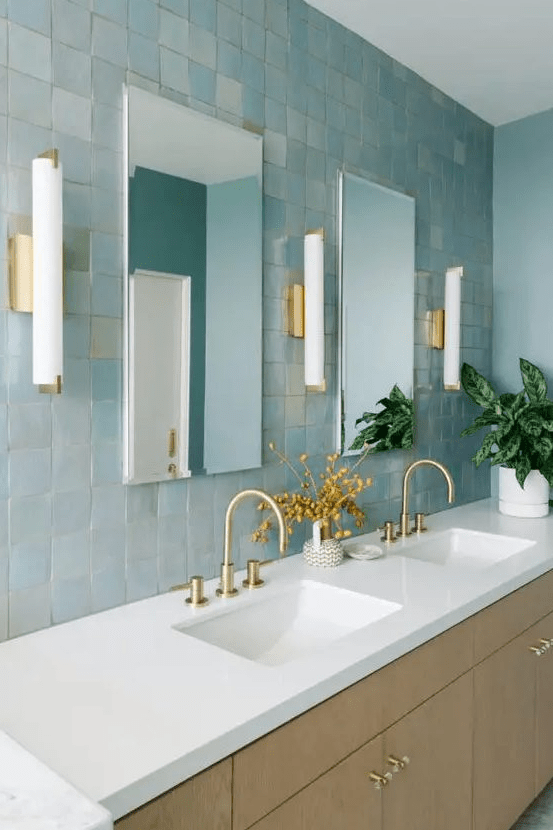 a blue bathroom clad with blue Zellige tiles, a large shared vanity with sinks, rectangular mirrors and sconces