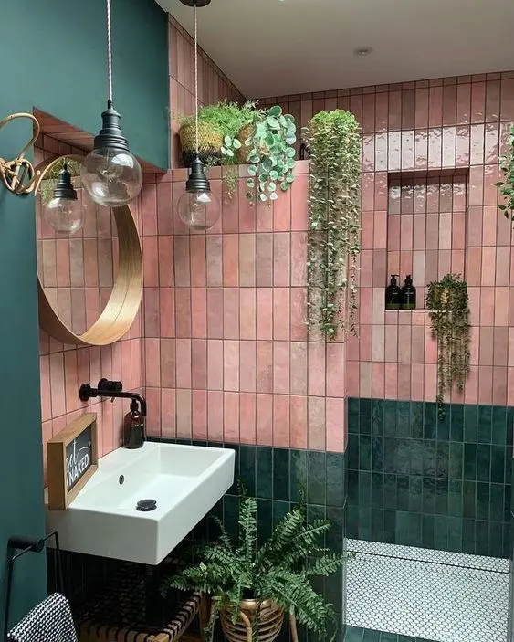 a bold green and pink bathroom done with stacked skinny Zellige tile, a shower space, a sink, potted greenery and pendant lamps