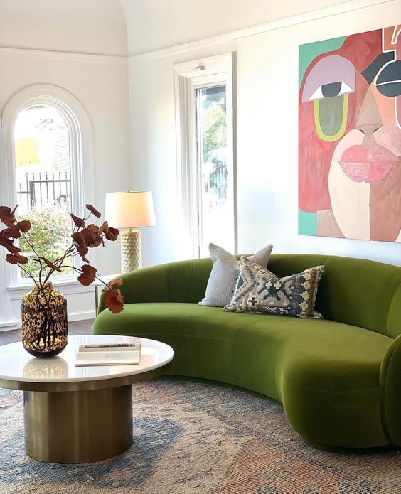 a bold living room with a green curved sofa, a coffee table, a bold artwork, a rug and some decor and pillows