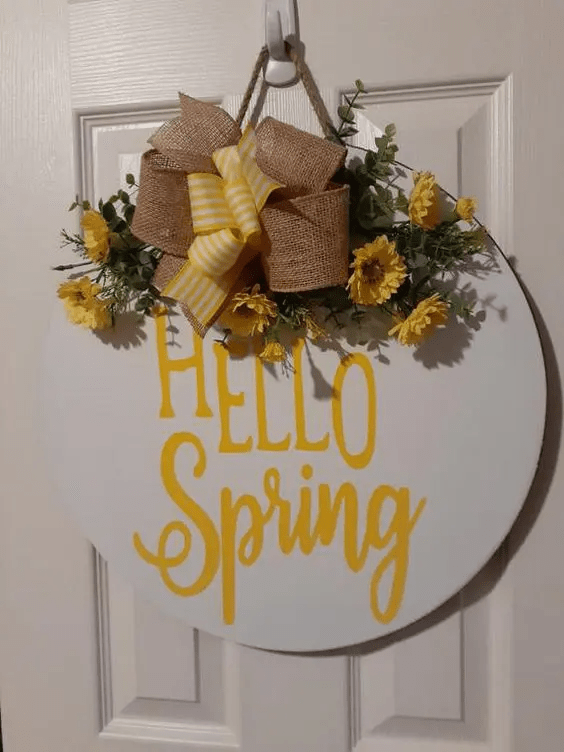 a bright spring sign with a striped and burlap bow, bright yellow blooms and greenery and yellow letters