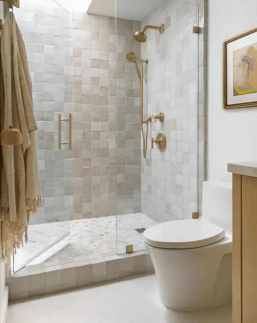 A catchy and light filled neutral bathroom clad with neutral Zellige tiles, a skylight over the shower, white appliances and gold fixtures