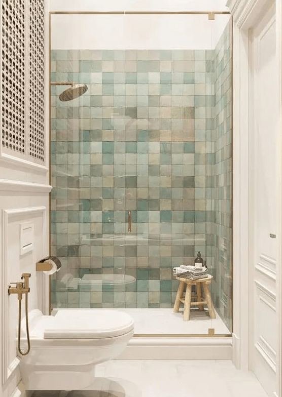 a chic modern bathroom with a shower space clad with blue and pink zellige tiles, brass fixtures and a skylight over the shower