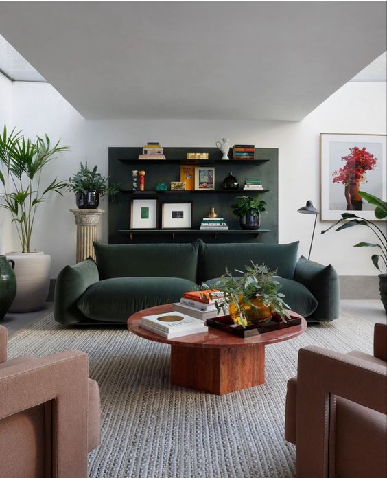 a chic modern living room with a dark green accent wall with decor, a dark green sofa, a stained table and mauve chairs is wow