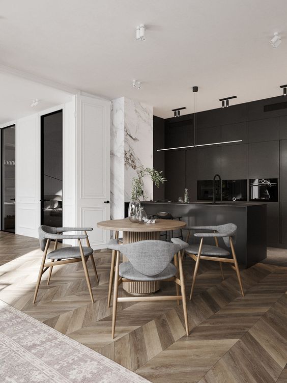 a chic modern space with a black kitchen, a chevron floor, a round table and grey chairs, lights and greenery