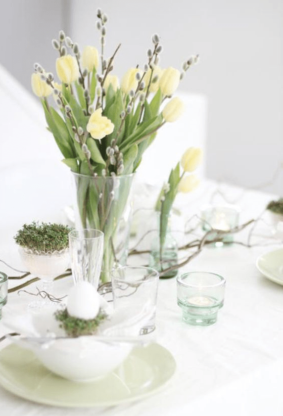 a clear vase with yellow tulips and willow, some branches and grass in a bowl is a lovely spring centerpiece to rock
