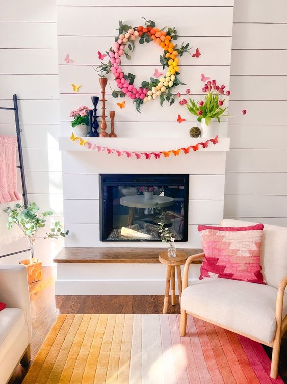 a colorful Easter mantel with a bright butterfly garland, a colorful egg wreath, pink tulips and potted blooms