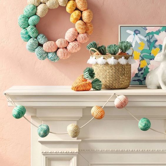 a colorful Easter mantel with a yarn egg garland, yarn carrots and a yarn egg wreath plus bunny figurines is a lovely idea