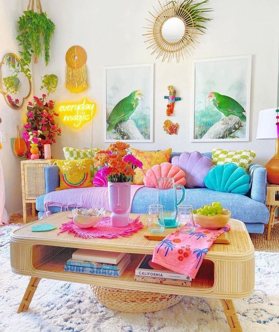 a colorful dopamine decor lviing room with a blue sofa and pastel and colorful pillows, a rattan coffee table, a neon sign, some art and greenery