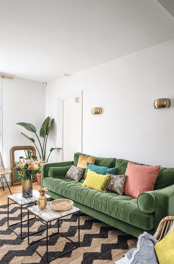 a colorful living room with a green sofa and bright pillows, a chevron rug, coffee tables, brass touches and potted plants