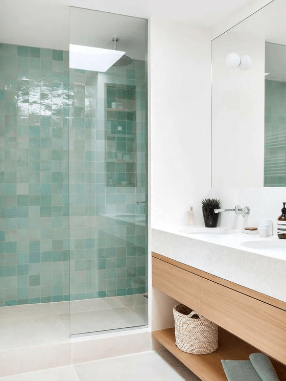 A contemporary bathroom in neutrals, with a shower space clad with green and turquoise Zellige tiles, a light stained vanity and a mirror