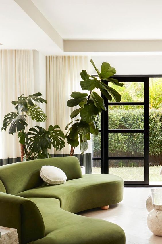 a contemporary living room with a green curved sofa, potted plants, color block curtains and an entrance to the garden