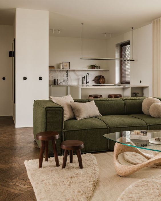 a contemporary open layout with a creamy kitchen, a living room zone with a green sofa, a glass coffee table and a cool rug