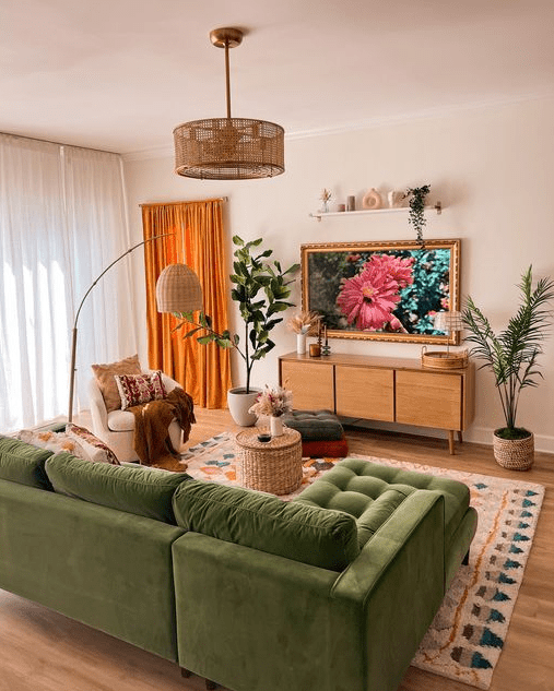 a cozy living room with a green sectional, a rug, a curved sofa, a side table, a TV unit, a woven chandelier and potted plants