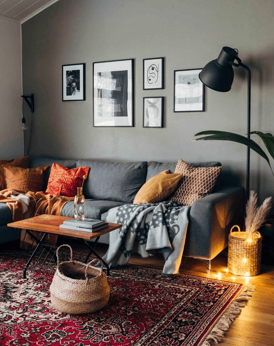 a cozy modern living room with a grey accent wall, a grey sofa with pillows, a black lamp, a gallery wall and a printed rug