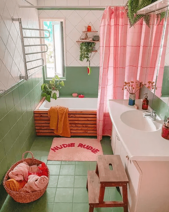 a dopamine decor bathroom clad with green and white tiles, a tub done with wood, a blush vanity, a pink curtain and rug