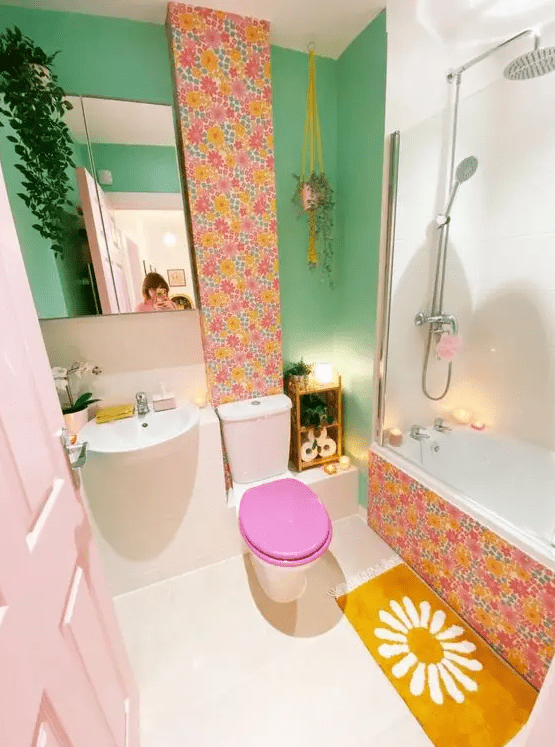 a dopamine decor bathroom with a green wall, wallpaper accents, a mustard rug, greenery and a blush door